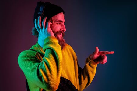 Listens to music, dances. Caucasian mans portrait on gradient studio background in neon light. Beautiful hipster male model in earphones. Concept of human emotions, facial expression, sales, ad.の写真素材