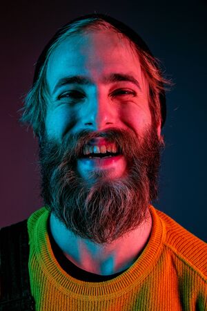 Laughting, smiling, close up. Caucasian mans portrait on gradient studio background in neon light. Beautiful male model with hipster style. Concept of human emotions, facial expression, sales, ad.の写真素材