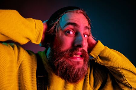 Exremely shocked, astonished. Caucasian mans portrait on gradient studio background in neon light. Beautiful male model with hipster style. Concept of human emotions, facial expression, sales, ad.の写真素材