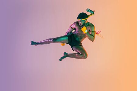 Muay thai. Young man exercising thai boxing on gradient background in neon light. Fighter...