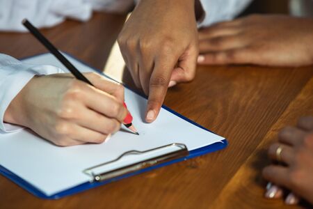 Close up of african-american and caucasian human's hands writing on wooden table. Female hands with the pencils noting something. Business, teamwork, studying, education, finance concept.の写真素材