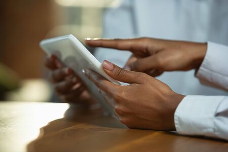 Close up of african-american humans hands using tablet on wooden table. Female hands touching blank screen, shopping online or serfing, browsing internet. Business, sales, online, finance concept.の写真素材