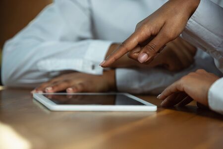 Close up of african-american humans hands using tablet on wooden table. Female hands touching blank...