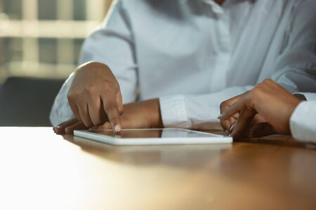 Close up of african-american humans hands using tablet on wooden table. Female hands touching blank...