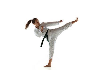 Confident junior in kimono practicing hand-to-hand combat, martial arts. Young female mongol fighter with green belt training on white studio background. Concept of healthy lifestyle, sport, action.の写真素材