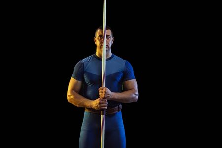 Male athlete practicing in throwing javelin on black background in neon light. Professional sportsman posing confident. Concept of healthy lifestyle, movement, activity, competition. Copyspace.の写真素材