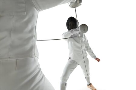 Teen girls in fencing costumes with swords in hands isolated on white studio background. Young...