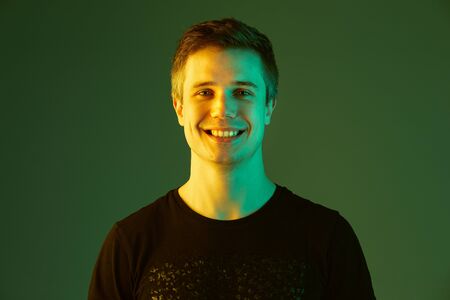 Smiling, looks happy. Close up. Caucasian mans portrait isolated on green studio background in neon...