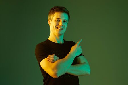 Pointing with hands crossed. Caucasian mans portrait isolated on green studio background in neon...