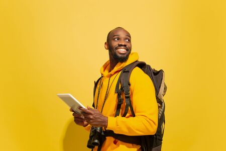 Using tablet, travel vlogging. Portrait of a cheerful young african-american tourist guy with bag...