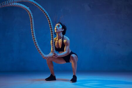 Caucasian young female athlete practicing on blue studio background in neon light. Sportive model...