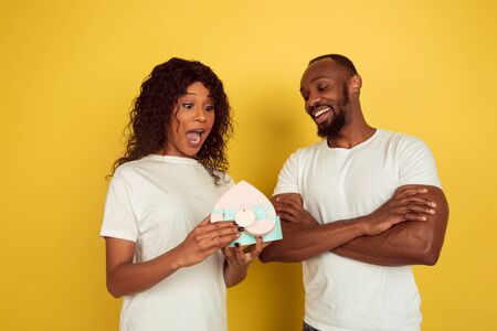 Happy to get gift. Valentines day celebration, happy african-american couple isolated on yellow studio background. Concept of human emotions, facial expression, love, relations, romantic holidays.の写真素材