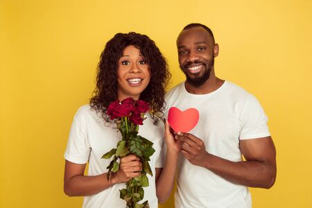 Flowers and heart. Valentines day celebration, happy african-american couple isolated on yellow studio background. Concept of human emotions, facial expression, love, relations, romantic holidays.の写真素材