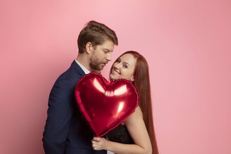 Happy holding balloons shaped hearts. Valentines day celebration, happy caucasian couple on coral...