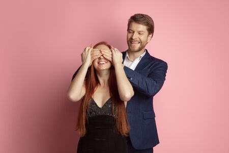 Surprising moment. Valentines day celebration, happy caucasian couple isolated on coral studio background. Concept of human emotions, facial expression, love, relations, romantic holidays.の写真素材