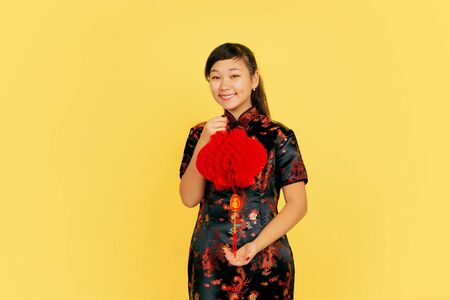 Posing with lantern, smiling, inviting. Happy Chinese New Year 2020. Asian young girls portrait on yellow background. Female model in traditional clothes looks happy. Celebration, emotions. Copyspace.の写真素材