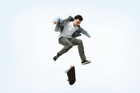 Caucasian young skateboarder riding isolated on a white studio background. Man in casual clothing training, jumping, practicing in motion. Concept of hobby, healthy lifestyle, youth, action, movement.の写真素材