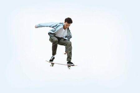 Caucasian young skateboarder riding isolated on a white studio background. Man in casual clothing training, jumping, practicing in motion. Concept of hobby, healthy lifestyle, youth, action, movement.の写真素材