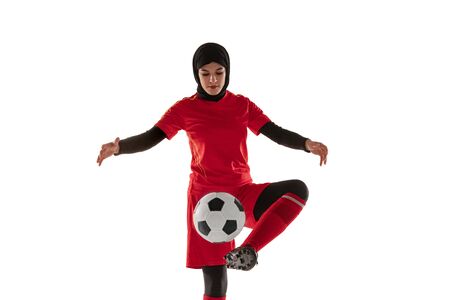 Arabian female soccer or football player isolated on white studio background. Young woman kicking the ball, training, practicing in motion and action. Concept of sport, hobby, healthy lifestyle.の写真素材