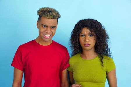 Close up of young emotional african-american man and woman in colorful casual clothes posing on blue...