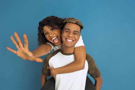 Young emotional african-american man and woman in white casual clothes posing on blue background....