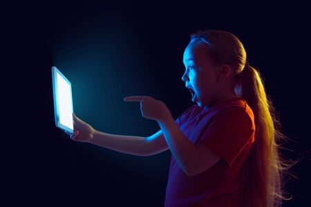 Pointing shocked. Caucasian girls portrait on dark studio background in neon light. Beautiful female...