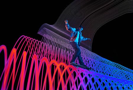 Caucasian young skateboarder riding on dark neon lighted line background. Training in action and...