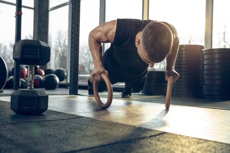 Flexible. Young muscular caucasian athlete training in gym, doing strength exercises, practicing,...