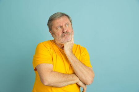 Thoughtful looking at side. Caucasian man portrait isolated on blue studio background. Beautiful male model in yellow shirt posing. Concept of human emotions, facial expression, sales, ad. Copyspace.の写真素材
