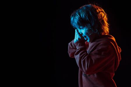 Cute talking on phone. Caucasian boys portrait on dark studio background in neon light. Beautiful curly model. Concept of human emotions, facial expression, sales, ad, modern tech, gadgets.の写真素材