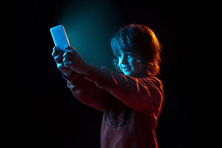 Open whole world with smartphone. Caucasian boys portrait on dark studio background in neon light....