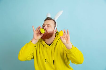 Egg hunt coming. Caucasian man as an Easter bunny with bright casual clothes on blue studio...