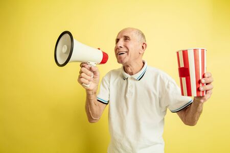Calling with mouthpeace. Caucasian senior mans portrait on yellow studio background. Beautiful male emotional model. Concept of human emotions, facial expression, sales, wellbeing, ad. Copyspace.の写真素材