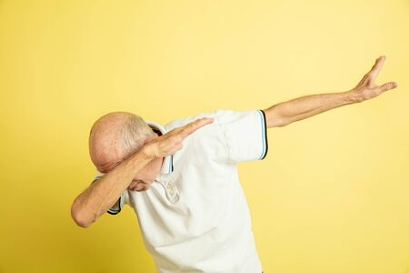 Dabbing, dab. Caucasian senior man's portrait isolated on yellow studio background. Beautiful male emotional model. Concept of human emotions, facial expression, sales, wellbeing, ad. Copyspace.の写真素材