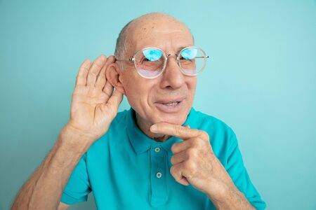 Listen to secrets. Caucasian senior mans portrait isolated on blue studio background. Beautiful male emotional model. Concept of human emotions, facial expression, sales, wellbeing, ad. Copyspace.の写真素材