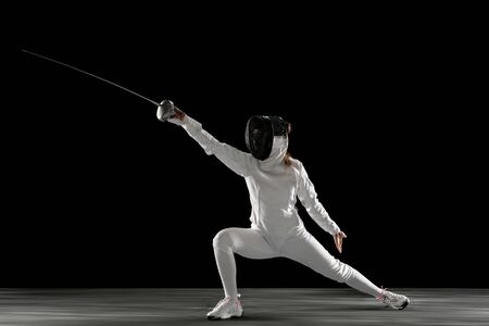 Targets. Teen girl in fencing costume with sword in hand isolated on black background. Young female...