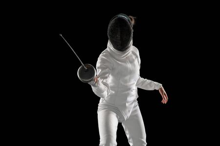 Invincible. Teen girl in fencing costume with sword in hand isolated on black background. Young...