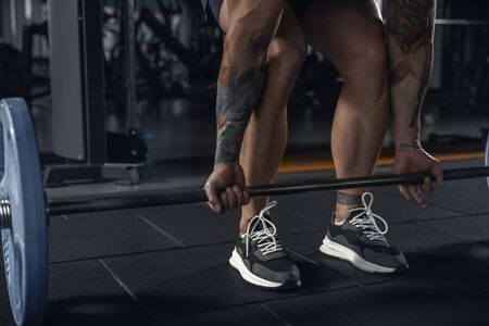 Powerful. Young muscular caucasian athlete practicing pull-ups in gym with barbell. Male model doing...