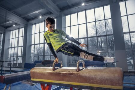 Prepared. Little male gymnast training in gym, flexible and active. Caucasian little boy, athlete in...