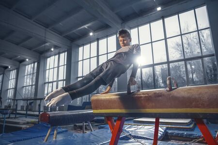 Prepared. Little male gymnast training in gym, flexible and active. Caucasian little boy, athlete in sportswear practicing in exercises for strength, balance. Movement, action, motion, dynamic concept.の写真素材