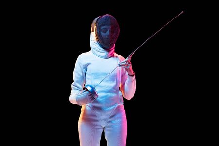 Ready. Teen girl in fencing costume with sword in hand isolated on black background, neon light....