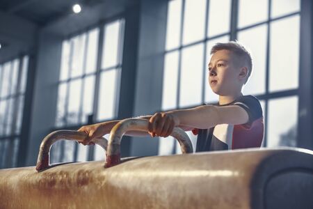 Ready. Little male gymnast training in gym, flexible and active. Caucasian little boy, athlete in sportswear practicing in exercises for strength, balance. Movement, action, motion, dynamic concept.の写真素材