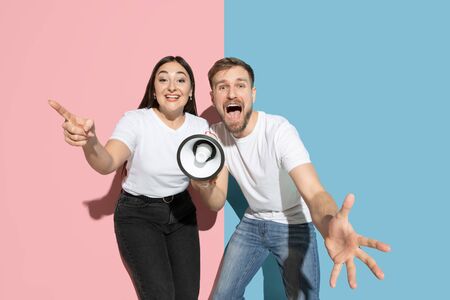 Together. Dancing, singing with megaphone. Young, happy man and woman in casual clothes on pink,...