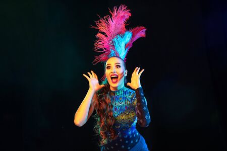 Surprised. Beautiful young woman in carnival, stylish masquerade costume with feathers on black...