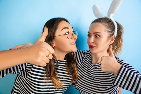 Thumbs up. Young emotional women isolated on gradient blue studio background. Concept of human emotions, facial expession, friendship, ad. Beautiful caucasian female models in casual clothes.の写真素材
