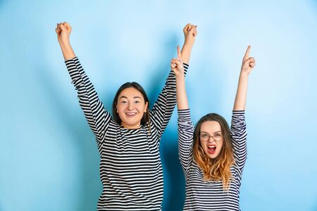 Happy winners, pointing. Young emotional women isolated on gradient blue studio background. Concept of human emotions, facial expession, friendship, ad. Beautiful caucasian models in casual clothes.の写真素材