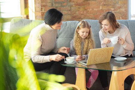 Comfortable. Happy loving family. Grandmother, mother and daughter spending time together. Watching cinema, using laptop, laughting. Mothers day, celebration, weekend, holiday and childhood concept.の写真素材