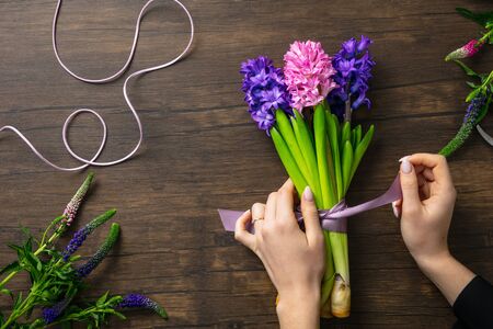 Florist at work: woman making fashion modern bouquet of different flowers on wooden background. Masterclass. Gift for bride on wedding, mothers, womans day. Romantic spring fashion. Emotional purple.の写真素材