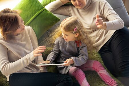 Comfortable. Happy loving family. Grandmother, mother and daughter spending time together. Watching cinema, using tablet, laughting. Mothers day, celebration, weekend, holiday and childhood concept.の写真素材