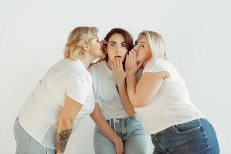 Secrets. Young caucasian women in casual clothes having fun together. Friends posing on white background and laughting, looks happy, well-kept. Bodypositive, feminism, loving themself, beauty concept.の写真素材